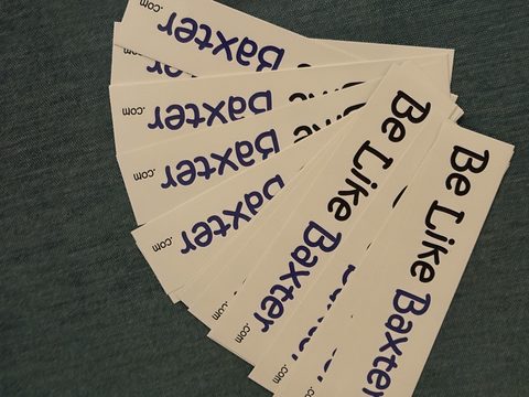 A fanned-out stack of Be Like Baxter bumper stickers, black and blue lettering on white